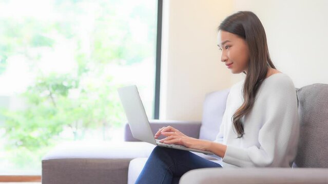 Close up of a young woman sitting on a couch typing on the laptop balanced on her legs.  Title space
