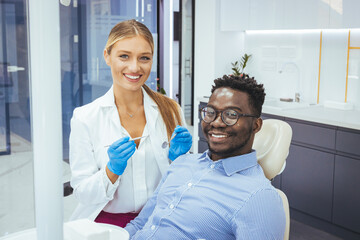 My dentist is the best! Portrait of a female dentist and young man in a dentist office. Happy dentist and patient in dentist's office. African guy in dentist chair smiling at camera, close up..
