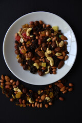 Assorted nuts on a white plate on a black background. A variety of delicious nuts on a plate.