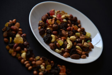 Assorted nuts on a white plate on a black background. A variety of delicious nuts on a plate.
