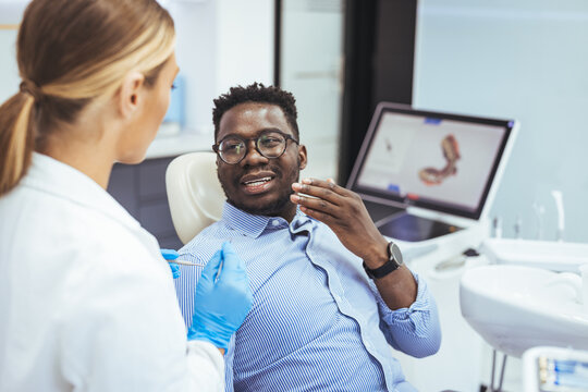 Unhappy african american man in medical chair complains of toothache to female dentist at modern dental clinic. Shot of a young man having a consultation with his dentist