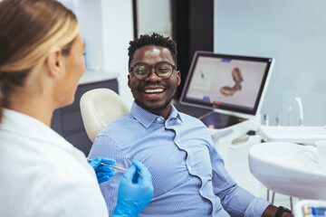 African American young man having a visit at the dentist's. He is sitting on chair at dentist...
