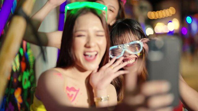 4K Group of Asian woman using mobile phone taking selfie together while celebrating and dancing at full moon beach party event. Female friends enjoy and fun outdoor summer travel vacation in Thailand