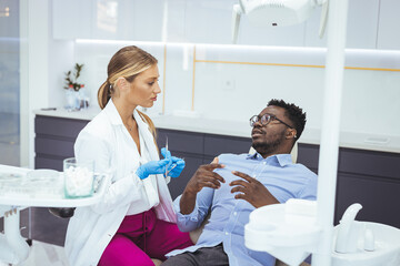 Female dentist with happy male patient at clinic. Happy patient sitting on chair while looking at dentist in medical clinic. Cheerful african american man with during examination in dental clinic