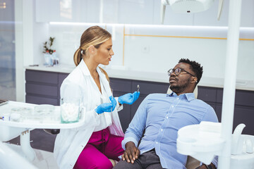 Obraz premium Young man patient having dental treatment at dentist's office. Female dentist working on patient's teeth. Man having teeth examined at dentists. Overview of dental caries prevention
