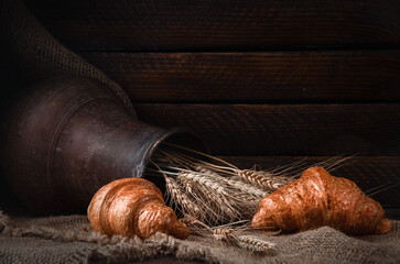 still life earthenware jug with wheat ears, bread, croissants on a drapery