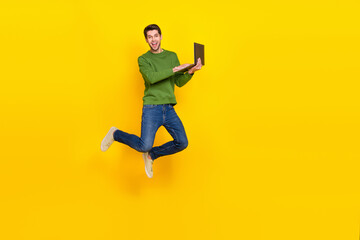 Fototapeta na wymiar Photo of pretty funky guy wear green sweater jumping high typing modern device empty space isolated yellow color background