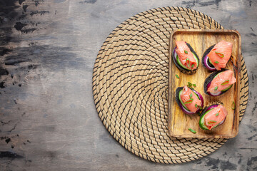 Smorrebrod, tapas or sandwich with onion, cucumber and salmon  on the cutting board. Top view Copy space