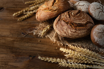 Freshly baked round bread and buns on burlap, on a wooden background. Next to the ears of wheat.
