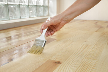 Varnishing of pine wooden plank floor or stairs, workers hand and paint  brush tool