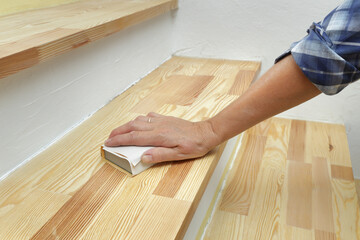 Fototapeta na wymiar Closeup of worker hand sanding wooden floor or stairs using hand tool