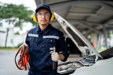 Portrait of an Asian mechanic holding a battery voltage meter in a car at a service station. Engine...