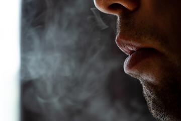 Male lips blowing smoke close-up, cigarette smoke and lips on black background.