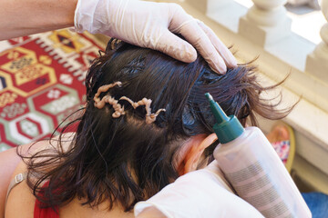 Gloved hands squeezing hair dye to woman's head for hair dyeing. Top or above view of organic hair coloring concept idea.