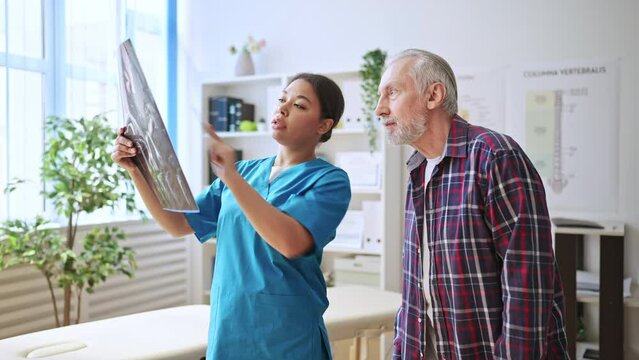 Physiatrist and her senior patient looking at x-ray image, healthcare specialist