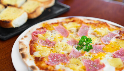 hawaiian thin crisp pizza has pineapple ham cheese and dill on top with garlic bread on white dish...