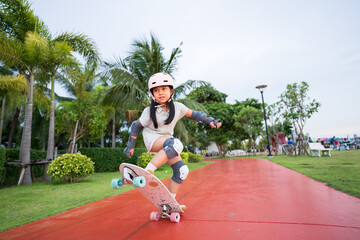 asian child skater or kid girl playing skateboard or surf skate and ollie jumping fun or raise wheel manual in skate park by extreme sports to wear helmet elbow pads wrist knee support for body safety © kornnphoto