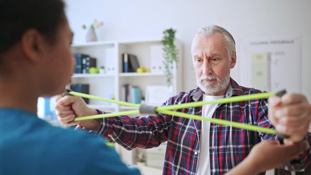 Senior male patient doing strengthening exercises with help of doctor, treatment