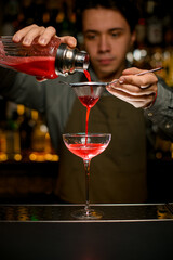 hand of male bartender holds sieve and pours cocktail through it into wine glass