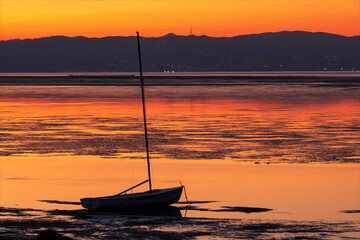 Paesaggio di mare con una barca a vela ormeggiata sulla laguna del mare della città isola di Grado alla mattina all'alba. Alba colorata di arancio con i monti sullo sfondo. 