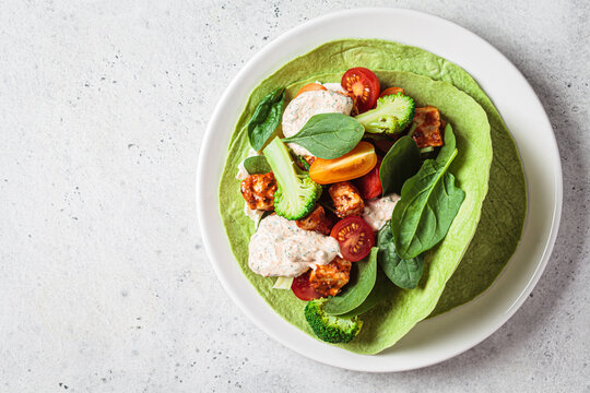 Open vegan tortilla wrap with broccoli, tofu and tomatoes. Vegetarian recipe, comfort food, plant-based concept.