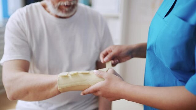 Closeup of female doctor fixing cast to senior man's hand, bone fracture, health