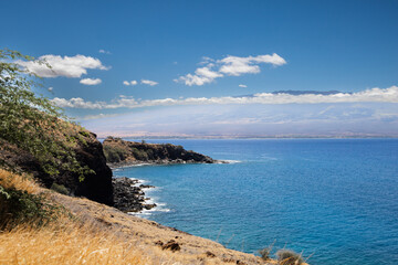 A high angle sweeping view of Maui Hawaii at mid day with a mountain, clouds and the Pacific ocean in the distance