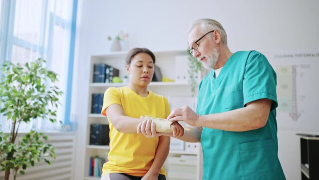 Doctor immobilizing bone in female patient's hand using plaster cast, injury