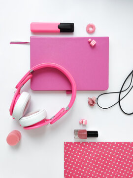 Pink female student accessories for study and recreation like headphones, marker, notepad, note, earrings lie on a white background