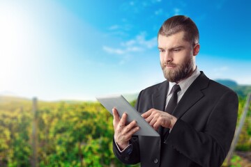 Happy farmer at the produce from his farm and using tablet for research in organic farm field. Agriculture or cultivation concept