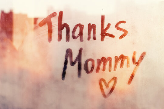 Handwritten text Thanks Mommy written finger with heart shape on orange sunset wet window