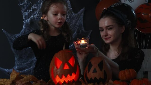 Two witches cast spells in the dark on Halloween on a black background with spider webs, autumn leaves and balloons. Halloween's holiday attributes. Trick or treat. Lantern carved from pumpkin known a