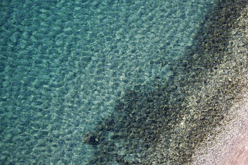 Transparent sea surface with pebble stones on a bottom, aerial view. Summer beach, turquoise water for background