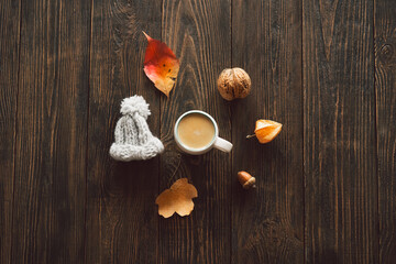 Autumn composition. Cup of coffee and autumn dried leaves, knitted little hat on wood background. Flat lay, top view