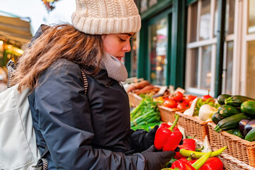 Woman buying peppers and vegetables from market stall.