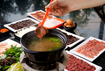 chopstick holding beef shabu-shabu or sukiyaki. Beef slice on top of hot pot, Fresh beef slices