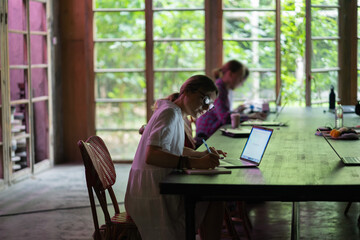 Young woman wearing glasses making notes, studying remotely in cafe, female student searching information in internet on laptop, watching webinar, learning foreign language online. Distance education