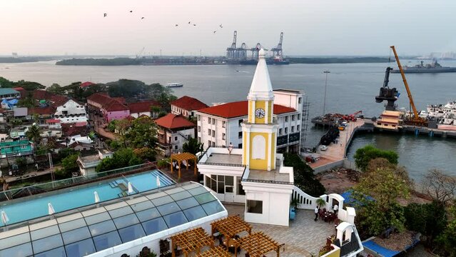 Aerial Panning Shot Of Clock Tower On Rooftop Cafe In City By Rippled Lake - Kochi, India