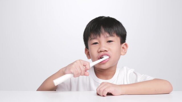 Asian kid brushing teeth with electric toothbrush. A 6 year old boy takes care of his bent baby tooth.