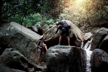  trekker tourist backpack ,hat with trekking stick . they show hold hand help adventure trekking at beautiful national park waterfall in summer vacation is eco tourism concept.