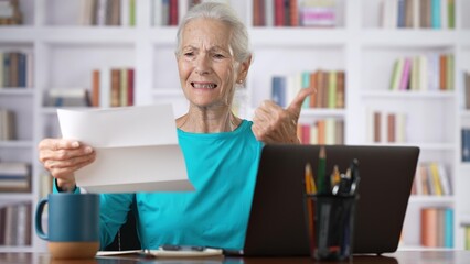 Senior elderly woman reading document paper notice letter from bank looking at smartphone nods head...