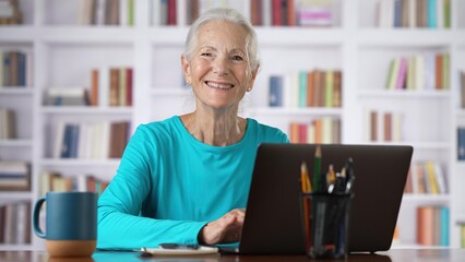 Portrait of elderly senior older woman on laptop looks up and smiles online concept, watching business training class, live webinar on laptop computer remote working, distance learning, home office.