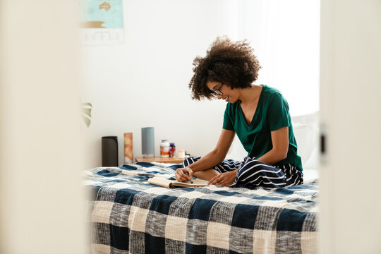 African american woman sitting in bed and drawing in sketchbook
