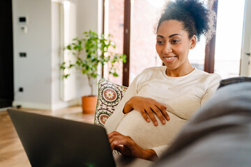 Adult beautiful pregnant smiling african woman working with laptop