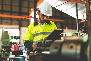 Young male engineer and worker checking and running a diagnostic test using electronic machine in factory and warehouse wearing uniform and hardhat to avoid malfunction in machines