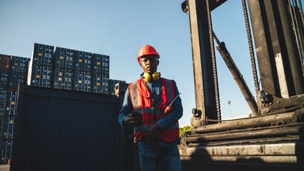 Young man with vest and helmet reading number of freight in warehouse