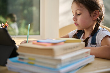 Adorable schoolgirl doing her homework with digital tablet at home. Child using gadgets to study. Education and distance learning for kids. Homeschooling during quarantine. Stay at home entertainment.