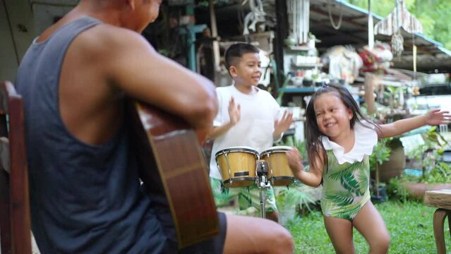 Happy Asian family on summer vacation. Grandfather with little grandchild boy and girl playing music and singing together at home. Senior man and children kid enjoy playing and dancing in the garden.
