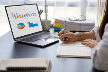 Asian businesswoman writing on paper and using laptop to searching data for working