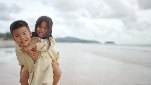 Happy Asian family on summer beach vacation. Little child boy and girl sibling walking together on the beach at summer sunset. Children kid enjoy and fun outdoor activity lifestyle playing at the sea
